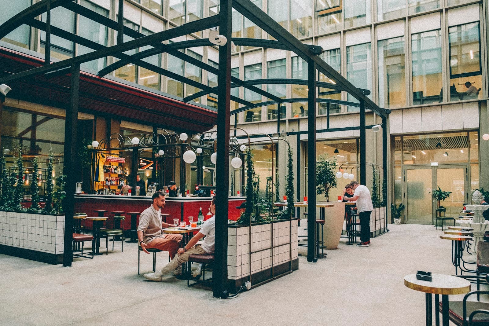 Interiorul barului Negroni Aperitivo, cu mese moderne, plante și oameni socializând la bar