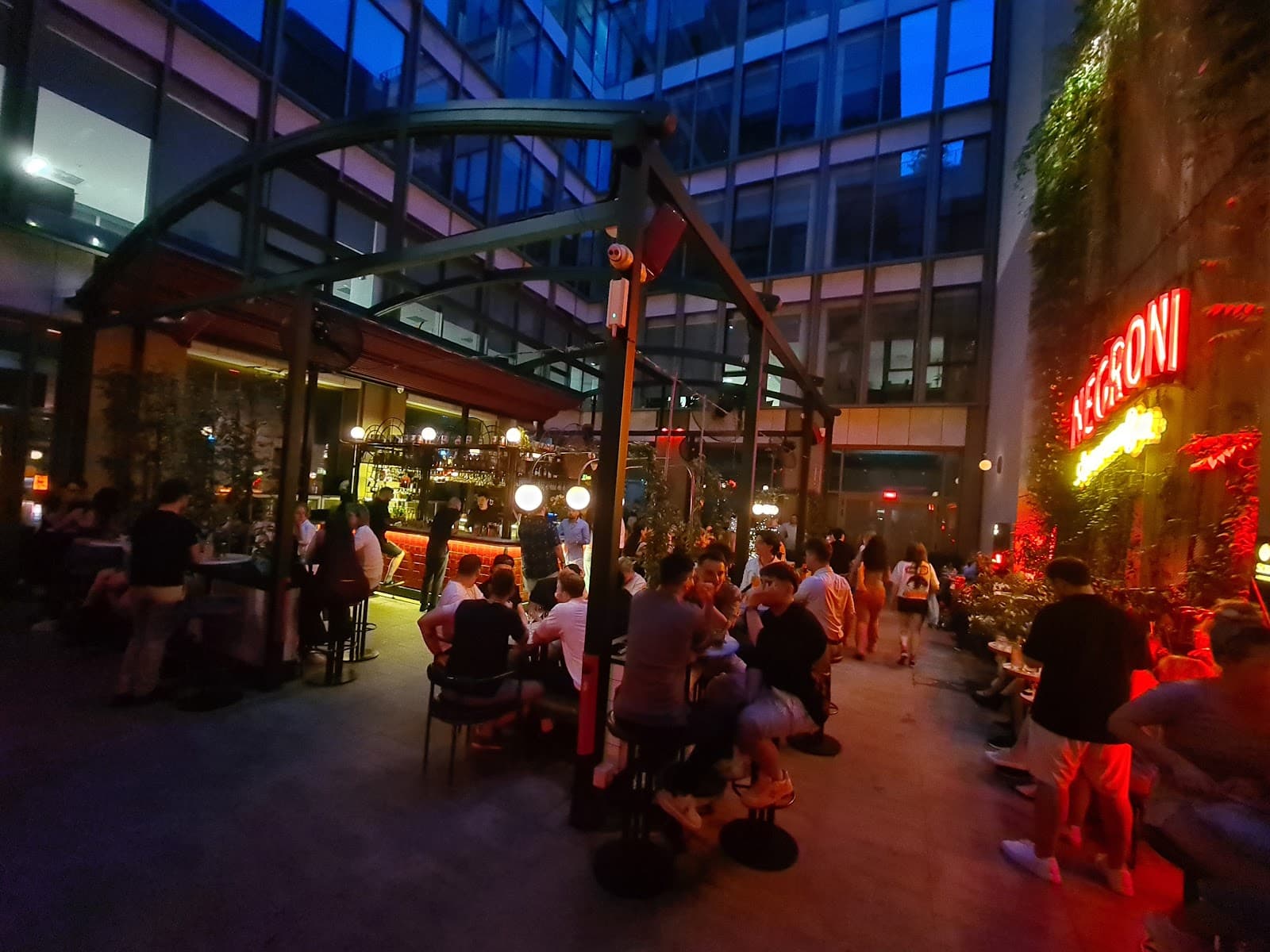 Terasa Negroni Aperitivo Bar seara, plină de lume, cu semnul neon roșu al barului