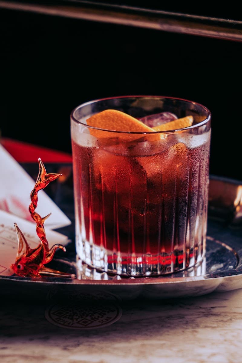 Cocktail roșu cu felii de portocală și gheață, pe o tavă metalică, pe masă de marmură