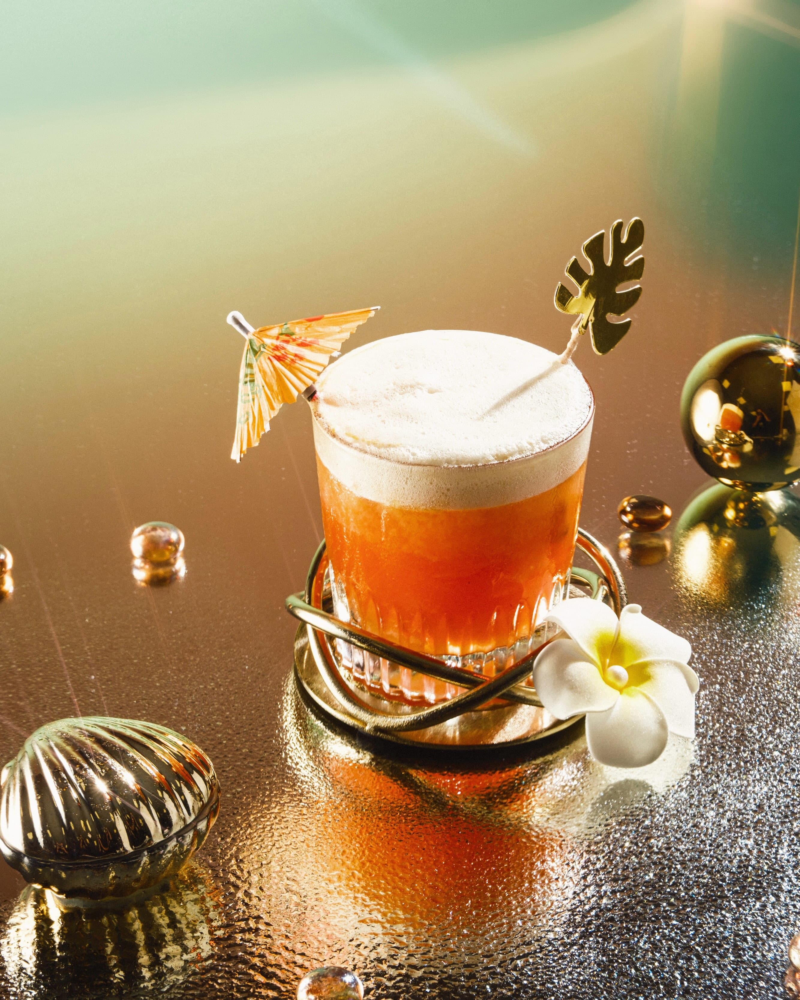 Cocktail cu spumă, decorat elegant, pe o masă reflectorizantă cu accente aurii